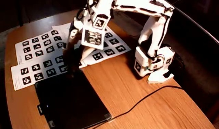 Overhead view of the SO-101 arm reaching over the drawing tablet.